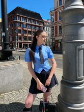 a lady wears a blue shirt with tie and a black mini pleated skirt